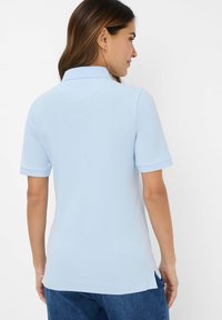 Lyseblå polo-tee med korte ærmer og krave. Glat tekstur, sidespidser ved kanten og en tætsiddende design. Minimalistisk detaljer.