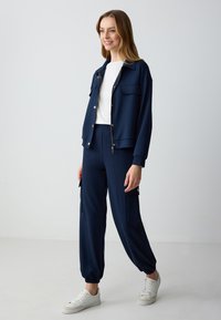 Navyblauwe trainingspak gemaakt van zachte stof, met een ritsjack met goudkleurige knopen en bijpassende broek met zijzakken en elastische boorden.