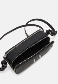 Sort crossbody taske med to lynlåslommer, blød lædertekstur, justerbar strop og logo detalje foran.