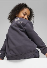 Sudadera gris oscuro hecha de tela suave, con un gráfico de una flor y una cara sonriente en la parte posterior, con dobladillos y puños acanalados.