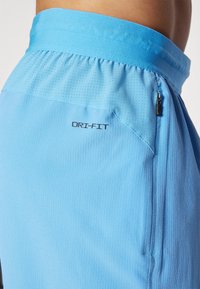 Vaaleansiniset urheilushortsit, jotka on valmistettu kosteutta imevästä kankaasta ribatulla tekstuurilla. Shortseissa on vetoketjullinen tasku ja sivussa "DRI-FIT" -logo.