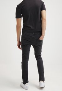 Jeans elásticos negros con corte slim, cinco bolsillos y costuras visibles, combinados con una camiseta negra ajustada y zapatillas blancas.