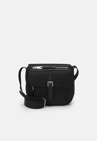 Černá crossbody taška se zlatým zipem a detaily přezky, nastavitelným širokým popruhem a přední kapsou na klopě na jednobarevném pozadí.