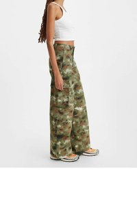 Spodnie cargo w kamuflażu w odcieniach zieleni, brązu i beżu z dużymi kieszeniami, szerokimi nogawkami i zamkiem błyskawicznym. Uzupełnione białym crop topem i trampkami.