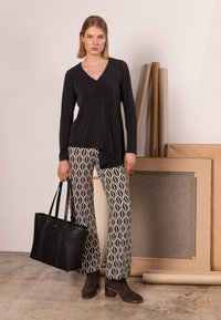 Černý dlouhý rukáv s výstřihem do V, vzorované široké kalhoty v krémové a námořnické modři, hnědé semišové boty na blokovém podpatku a strukturovaná černá taška přes rameno.