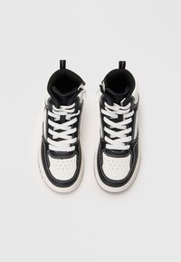 Υψηλές αθλητικές κάλτσες από λευκό και μαύρο δέρμα, με λευκές κορδόνες, στρογγυλή μύτη, αντιθετική ραφή και μαλακή γλώσσα στο πίσω μέρος.