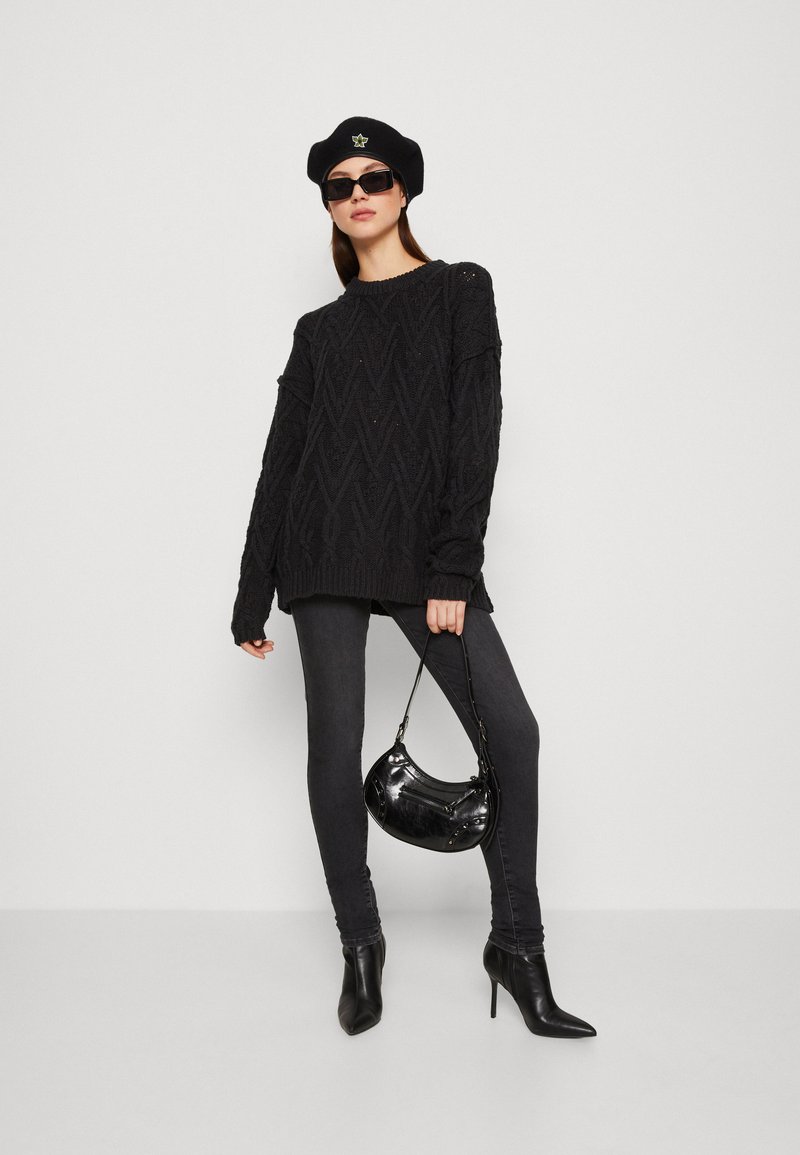 Un pull noir en tricot avec un motif en losanges texturé, associé à un jean skinny foncé et des bottes à talons aigus noires. Les accessoires comprennent un béret noir et des lunettes de soleil.