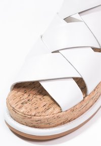 Sandale blanche avec larges brides croisées en cuir et semelle plateforme en liège texturé avec une semelle en caoutchouc blanc et marron.