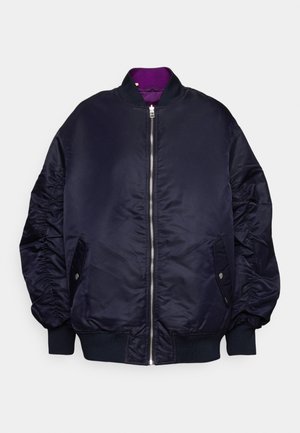 Chaqueta bomber azul marino con cremallera frontal, puños y dobladillo acanalados, bolsillos laterales con solapa y botones, y forro morado visible en el cuello.