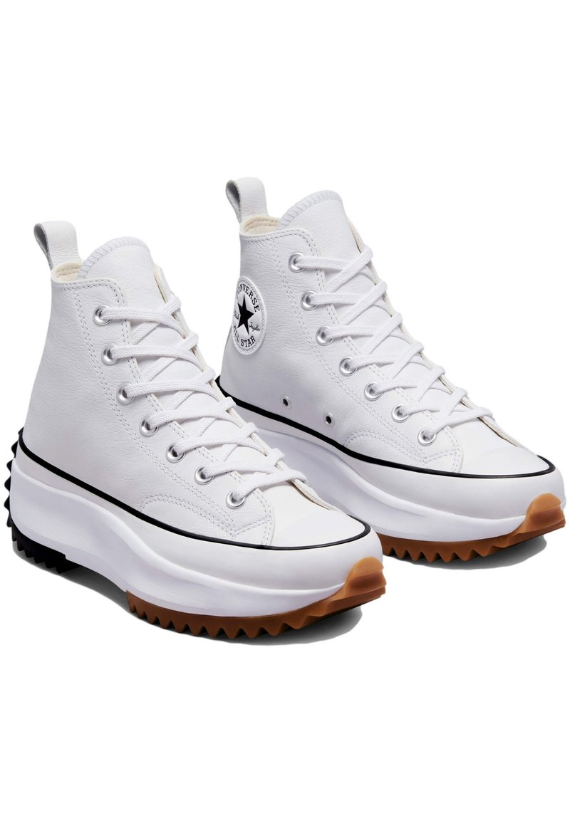 Baskets montantes en cuir blanc avec semelle en caoutchouc texturée, accents noirs et patch logo. Comprend cinq œillets et une conception de chaussure à bout rond.