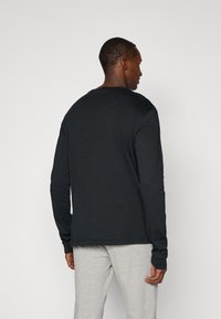Black long-sleeve shirt in a relaxed fit, made of cotton, featuring a round neck and simple design, paired with grey pants.