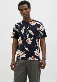 Tamsiai mėlynas trumpomis rankovėmis marškinėliai su dideliu gėlių raštu kreminės, raudonos ir žalios spalvos. Apvalus kaklas ir laisvas kirpimas, pagaminti iš švelnios medžiagos.