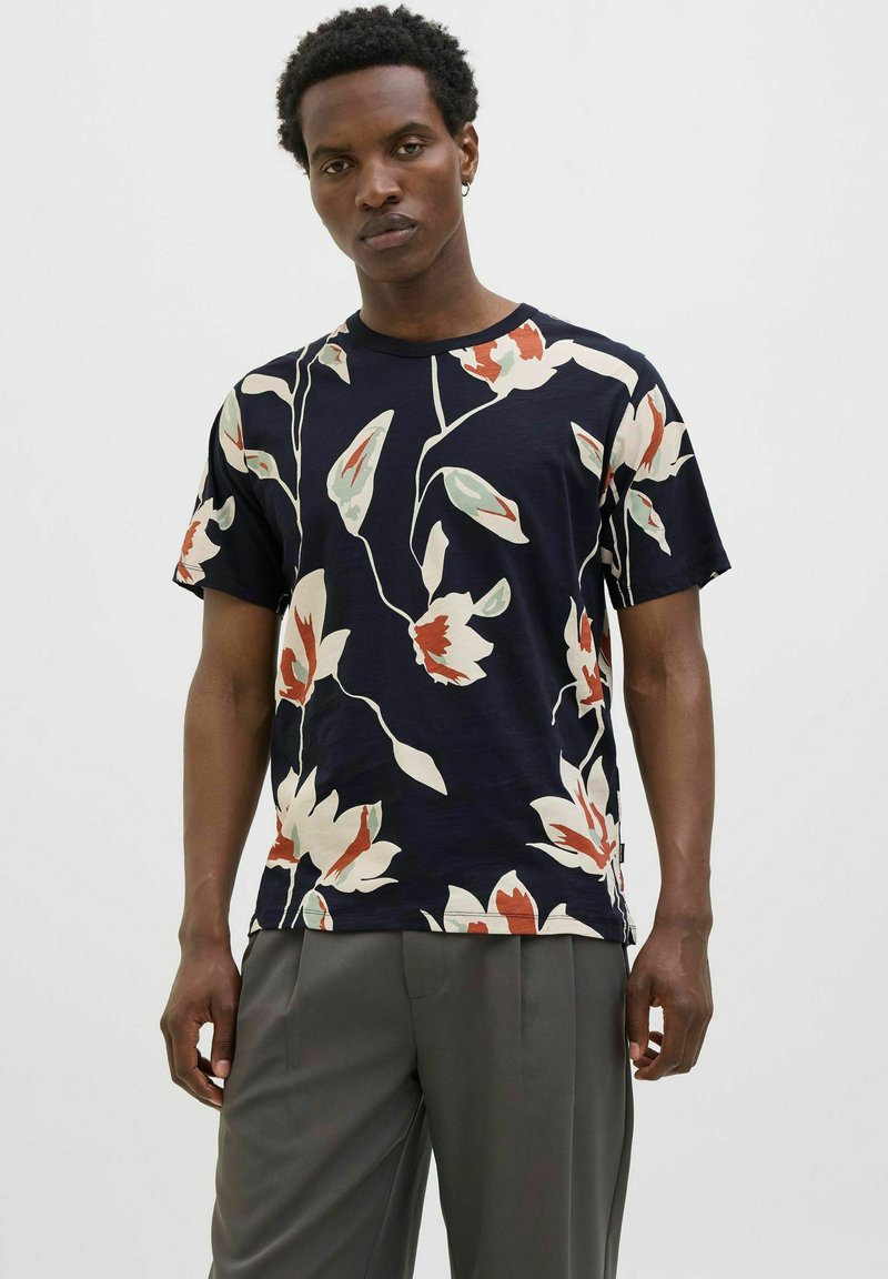 Tamsiai mėlynas trumpomis rankovėmis marškinėliai su dideliu gėlių raštu kreminės, raudonos ir žalios spalvos. Apvalus kaklas ir laisvas kirpimas, pagaminti iš švelnios medžiagos.