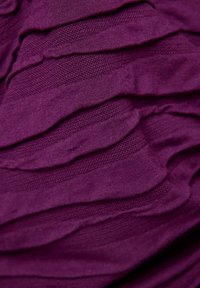 Texturiertes lila Gewebe mit geschichteten Volants, das eine Kombination aus glatten und gerippten Abschnitten aufweist, wodurch Tiefe und visuelles Interesse entstehen.
