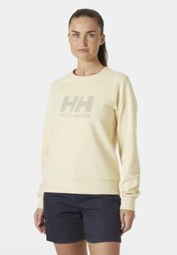 Sudadera amarilla de manga larga, cuello redondo, con un logo "HH" en gris claro, combinada con pantalones cortos azul marino. Textura de tela suave.