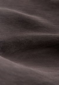 Tissu brun foncé lisse avec des plis subtils et une texture fine, doucement éclairé pour montrer la profondeur et les détails du matériau.
