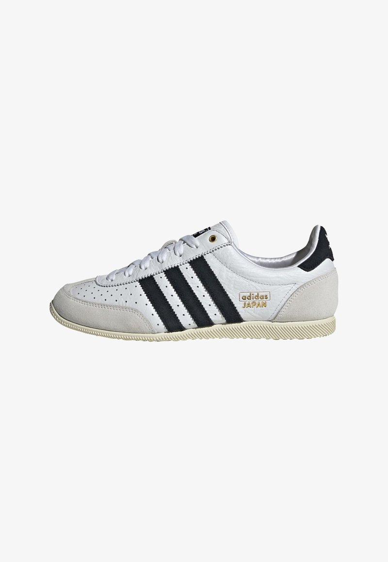 Hvit sneaker med svarte striper og gullmerke. Har semsket og lærmaterialer, perforert overdel og teksturert gummisåle.