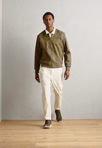Suede bomber jacket in olive green, white collared shirt, cream pants, and dark green sneakers, with a modern fit and smooth texture.