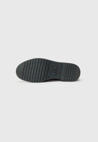 Rubber shoe sole, dark gray color, textured with horizontal grooves and vertical lines for traction, featuring a logo near the heel.