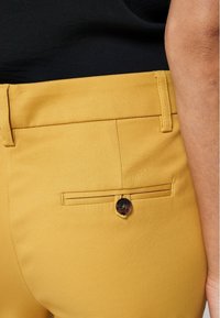 Pantalons en coton jaune avec une poche arrière ornée d'un bouton décoratif et une texture lisse. Conçus dans une coupe classique avec des lignes épurées.
