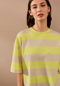 Mikina s krátkym rukávom s horizontálnymi pruhmi v jasne žltej a béžovej farbe. Hladká bavlnená látka s voľným strihom a okrúhlym výstrihom.