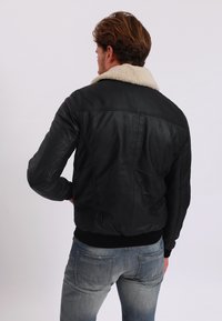 Černá kožená bomber bunda s krémovým beránkovým límcem a žebrovanými manžetami. Zadní strana má hladký povrch s minimálními švy.