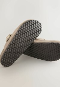 Zapatos de ante color topo con parte superior en el mismo tono y suela de goma negra texturizada con un patrón de panal. Incluye un sencillo detalle de hebilla metálica.