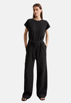 Completo nero con maniche corte, vestibilità ampia, vita con lacci, tasche laterali e tasca sul petto. Realizzato in un tessuto morbido, design minimalista.