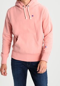 Lichtroze sweatshirt met capuchon, kangoeroezak en trekkoorden. Heeft een klein blauw logo op de borst en geribbelde boorden aan de mouwen en zoom.