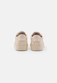 Beige lädersneakers med en slät yta, rundad baksidesdesign och diskret sömnadsdetaljering på häl och sidor.