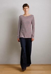Rød og hvitstripet langermet topp kombinert med mørke, vide jeans. Stoffet ser glatt ut, og designet har en vid utringning.