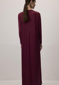 Longue robe bordeaux en tissu doux, avec manches longues et coupe décontractée, sans motifs ni éléments métalliques apparents.