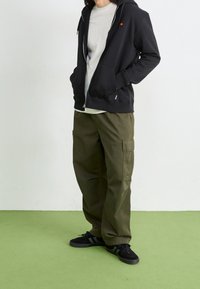 Czarna bluza z kapturem na zamek, na jasnoszarej koszulce, w połączeniu z oliwkowozielonymi spodniami cargo i czarnymi trampkami z zielonymi paskami.