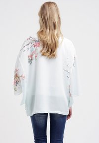 Transparente weiße Kimono-Oberteil mit Blumenmustern in Pink und Blau, mit weiten Ärmeln und einem lockeren, fließenden Design.