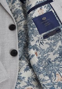 Blazer grigio chiaro con due bottoni neri e fodera a motivo floreale in tonalità di blu navy, crema e arancio. Etichette visibili all'interno.