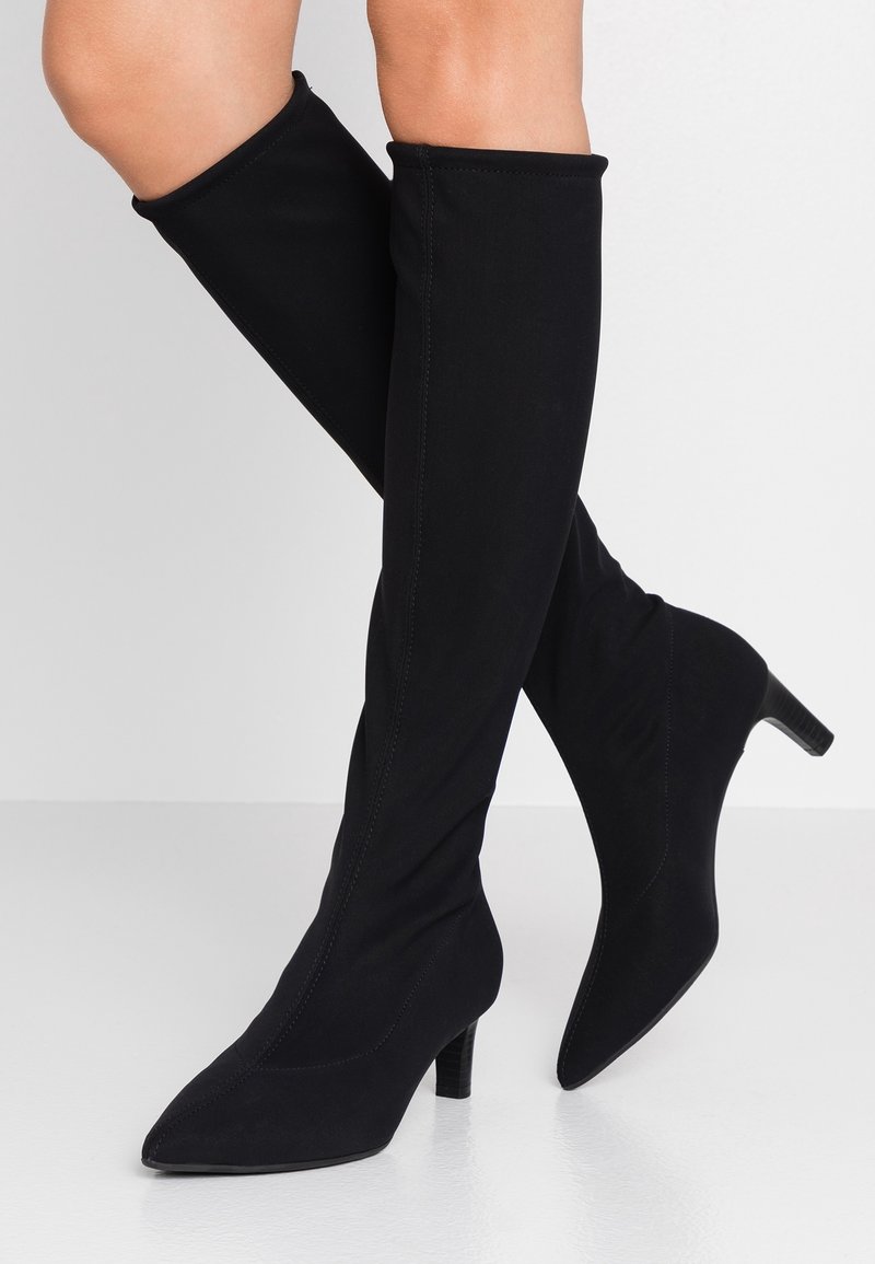 Bottes montantes noires en tissu doux et extensible, avec un bout pointu et un talon modeste orné de surpiqûres décoratives le long des coutures.
