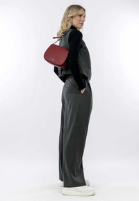 Gray tailored vest and wide-leg pants, paired with a red leather crossbody bag. Model wears white sneakers, hair down. Plain background.