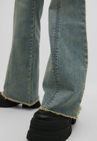 Pantalones vaqueros acampanados de denim azul con dobladillo deshilachado y costuras en contraste, combinados con chunky black platform shoes.
