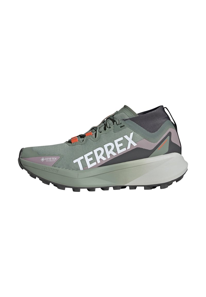 Basket de sport verte avec une tige en mesh texturé, accents gris clair et noir, logo "TERREX" bien en vue, lacets orange et semelle extérieure robuste.