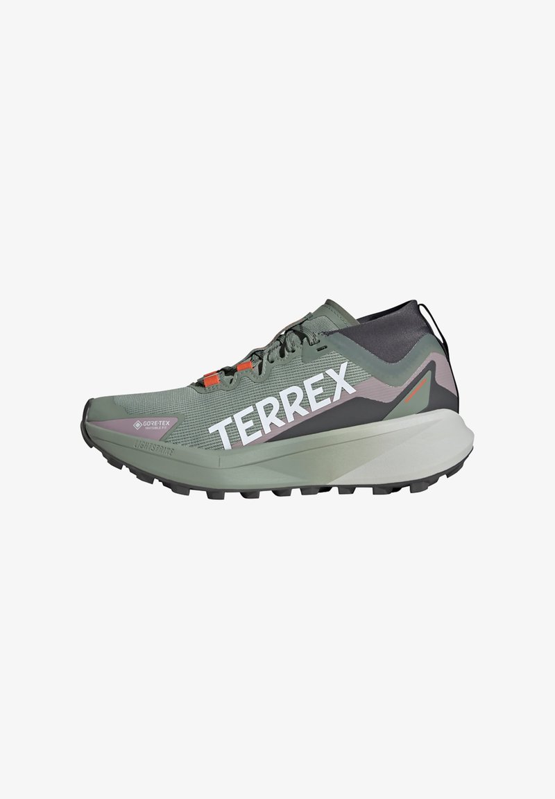Zaļas sporta apavus ar teksturētu sieta augšdaļu, gaiši pelēkiem un melniem akcentiem, izteiksmīgu "TERREX" logotipu, oranžām šņorēm un izturīgu zoli.