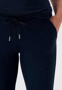 Marineblauwe joggers gemaakt van zachte stof, met een trekkoord in de taille met zilveren metalen uiteinden en zijzakken.