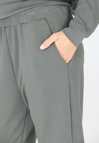 Zachtgrijze, losse sweatpants gemaakt van zacht materiaal, met een elastische tailleband en zijzakken. Subtiele textuur zichtbaar.