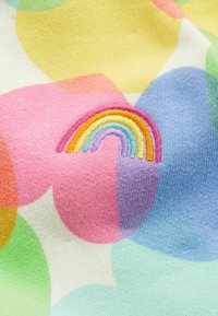 Gebreide stof met een pastelkleurenpalet en grote overlappende vormen. Bevat een gestikte regenboogdetail in levendige kleuren.