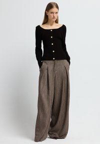 Schwarzer gerippter Pullover mit weitem Ausschnitt und goldenen Knöpfen, kombiniert mit lockeren, strukturierten braunen Schlaghosen mit vorderen Falten.