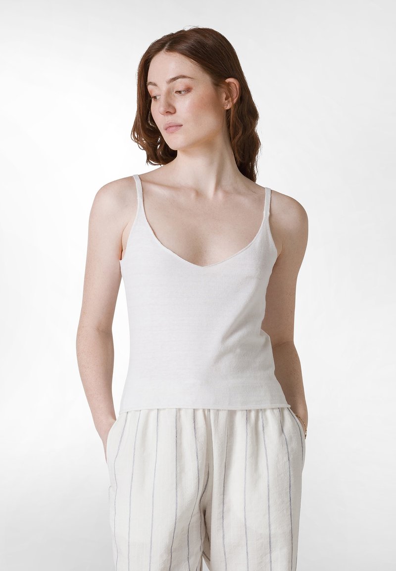 Witte katoenen tanktop met dunne banden, v-hals en aansluitende silhouet, gecombineerd met losse, lichtgekleurde linnen broek met verticale strepen.
