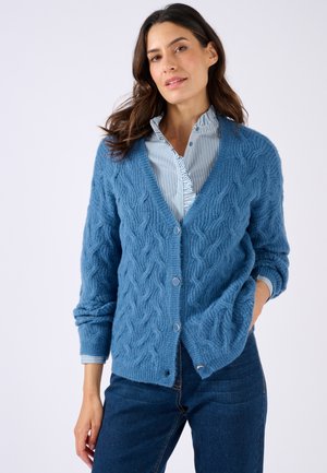 Blauwe gebreide cardigan met een getextureerd kabelpatroon, V-hals en knopen aan de voorkant. Gepaard met een gestreepte shirt en spijkerbroek.