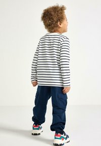 Langärmliges gestreiftes T-Shirt in Weiß und Marineblau, kombiniert mit Marineblauen Cargo-Hosen und mehrfarbigen Sportschuhen. Mit Rundhalsausschnitt und lockerer Passform.
