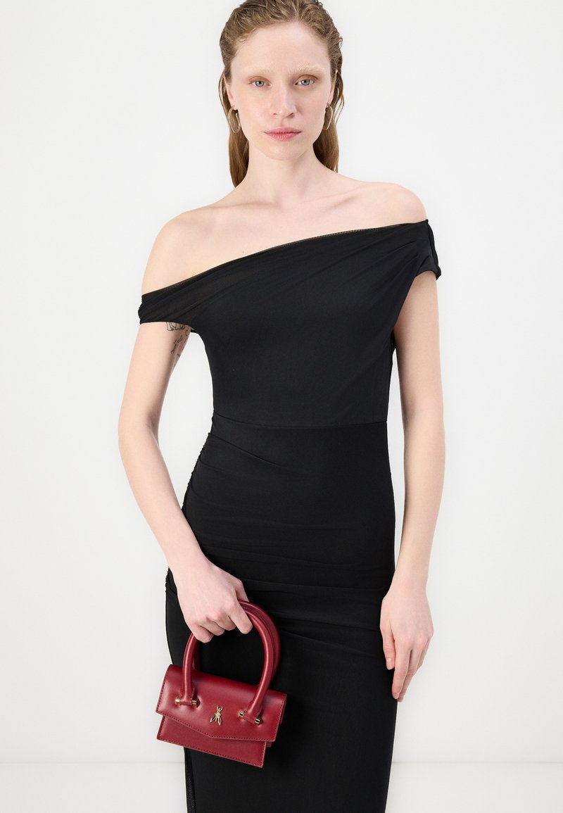 Zwarte off-shoulder jurk met een getailleerde snit en een zachte textuur. Het model houdt een kleine rode leren handtas met een gestructureerd ontwerp vast.