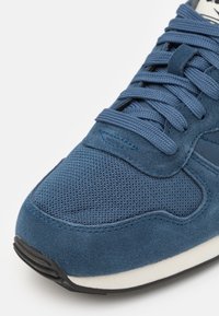 Blue sneaker featuring a textured mesh and suede upper, flat laces, and a black rubber sole with a slight white accent.
