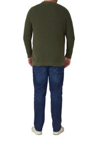 Zielony oliwkowy sweter w prążki z okrągłym dekoltem, zestawiony z niebieskimi dżinsami i kremowymi trampkami, widziany od tyłu.